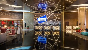 Un vestíbulo moderno con una instalación de luces geométricas, un mostrador de recepción y zonas de estar.