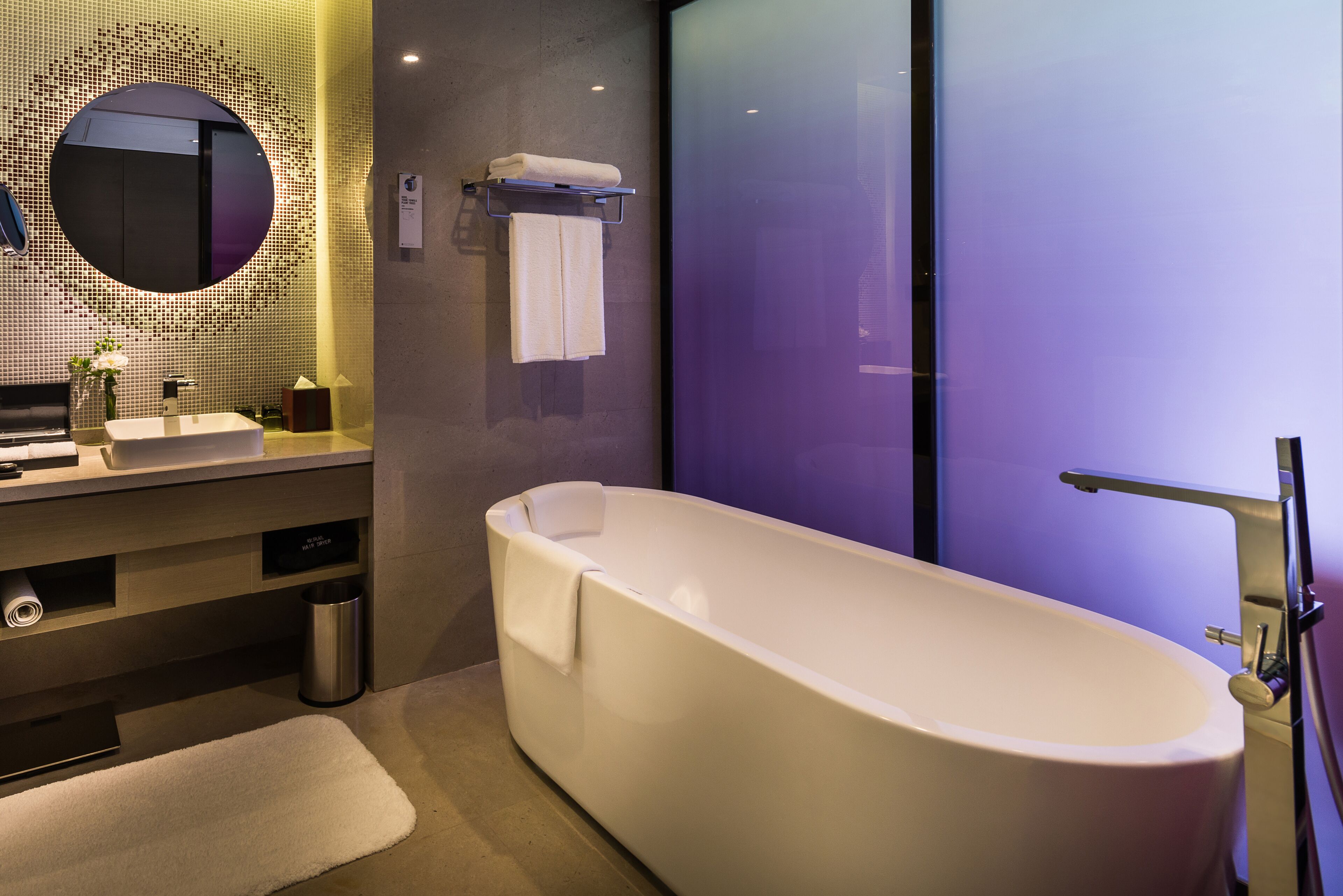 A modern bathroom with a freestanding bathtub, a round mirror, and a sink with a towel rack.