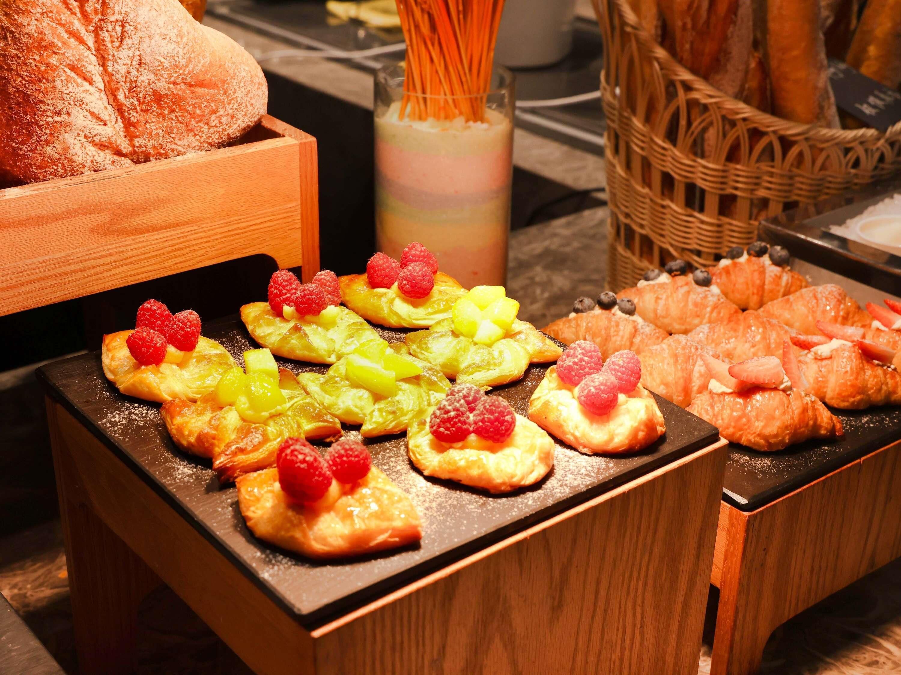 A variety of pastries and bread displayed on a wooden table, with baskets of bread in the background.