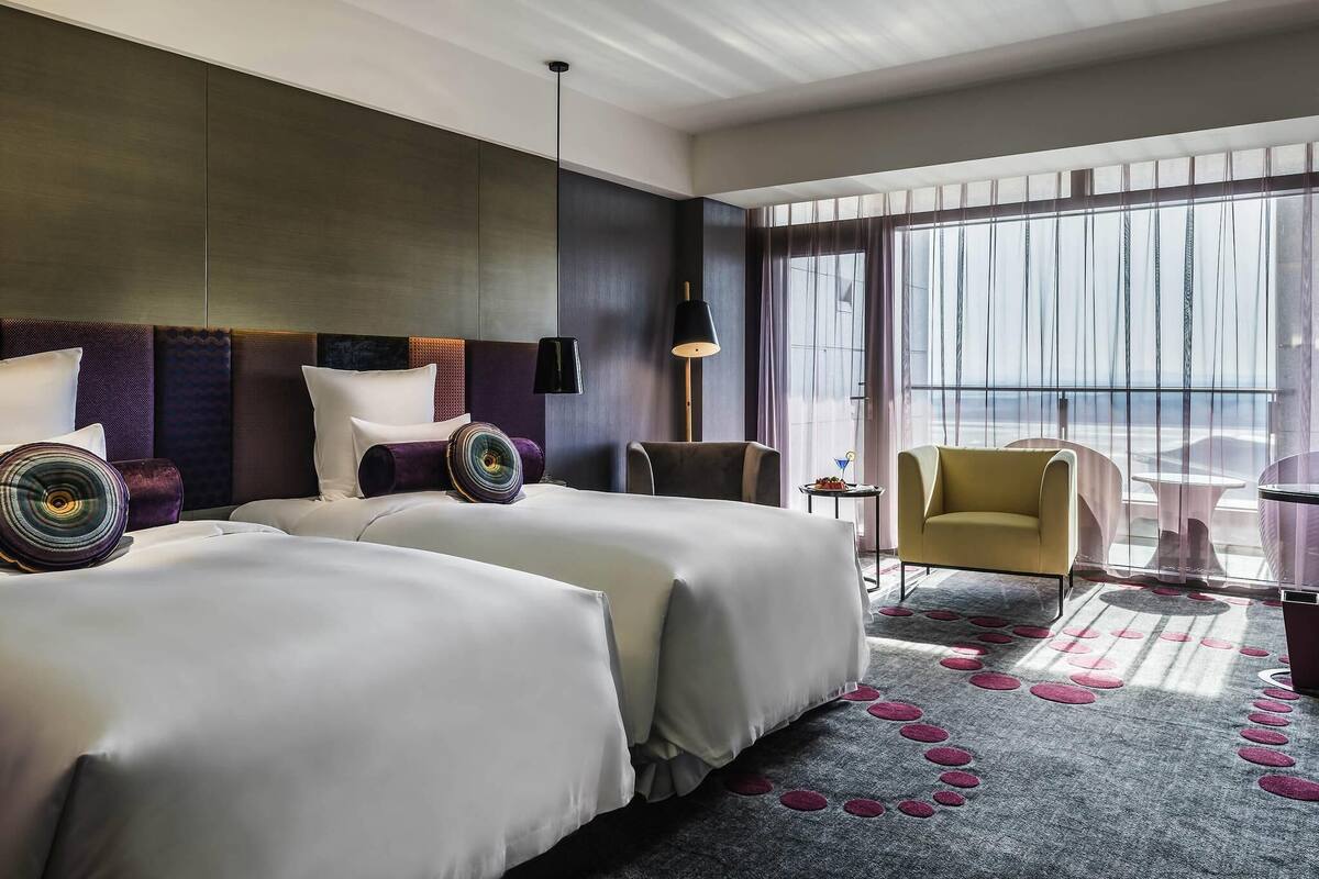 Una habitación de hotel con dos camas, un ventanal amplio, una silla y una mesita.