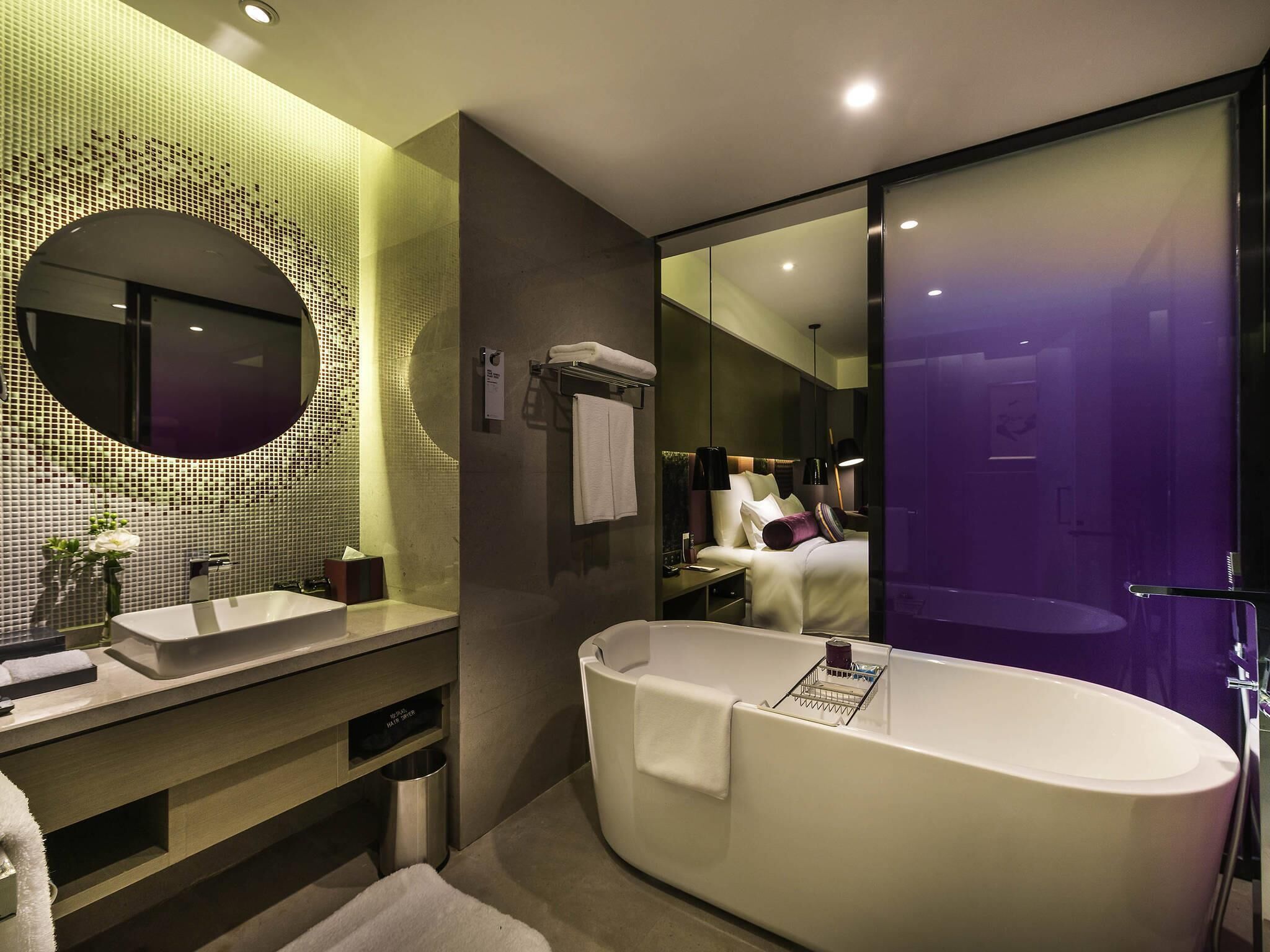 Un baño moderno con una bañera independiente, un espejo redondo y un tocador con lavamanos y toallero.