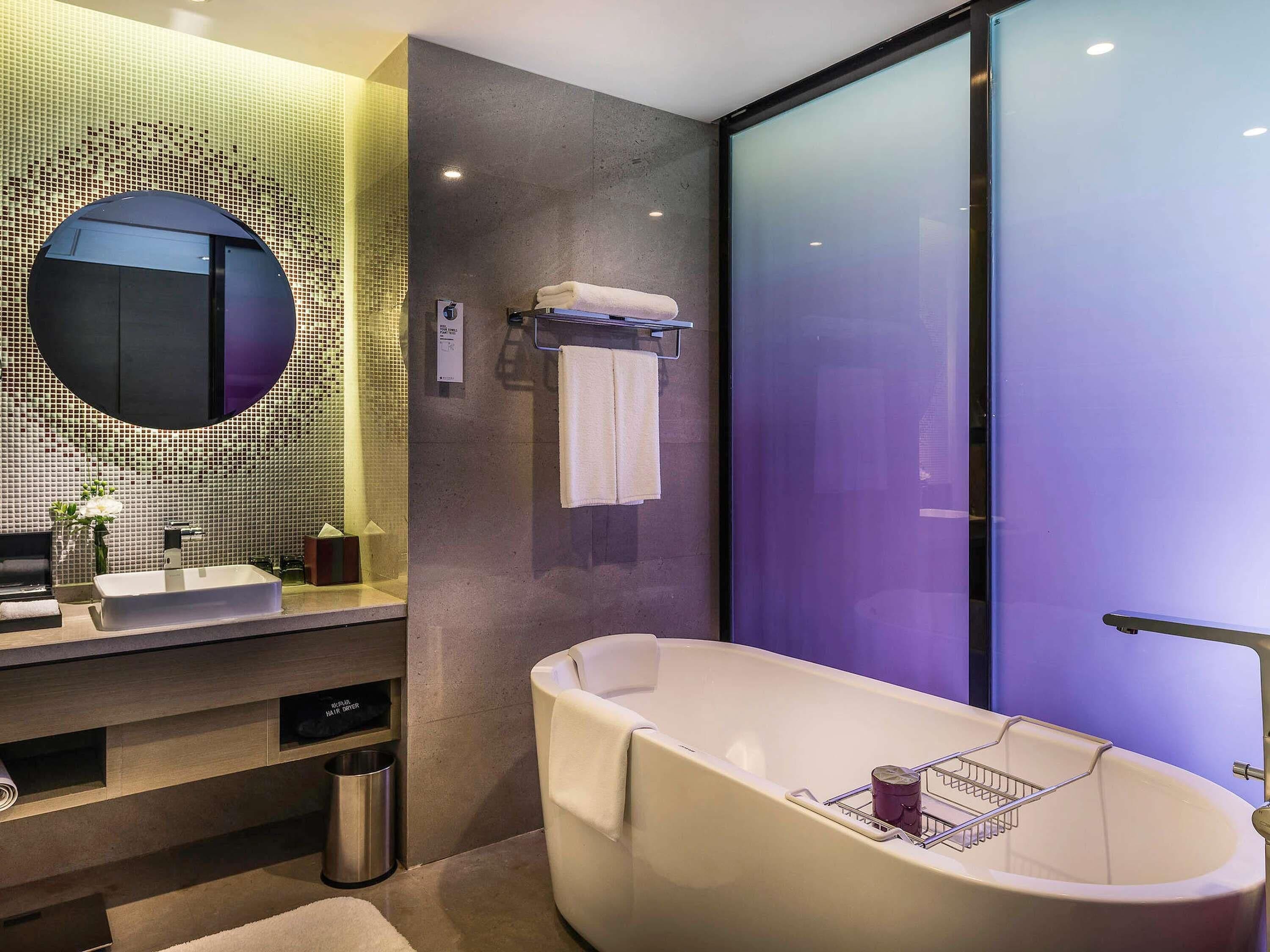 A modern bathroom with a freestanding bathtub, a round mirror, and a tiled wall.