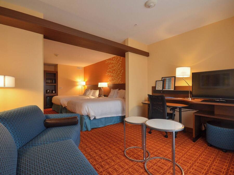 Ein Hotelzimmer mit einem Bett, zwei Nachttischen, einem Schreibtisch mit Stuhl, einem Fernseher und einem Sofa.