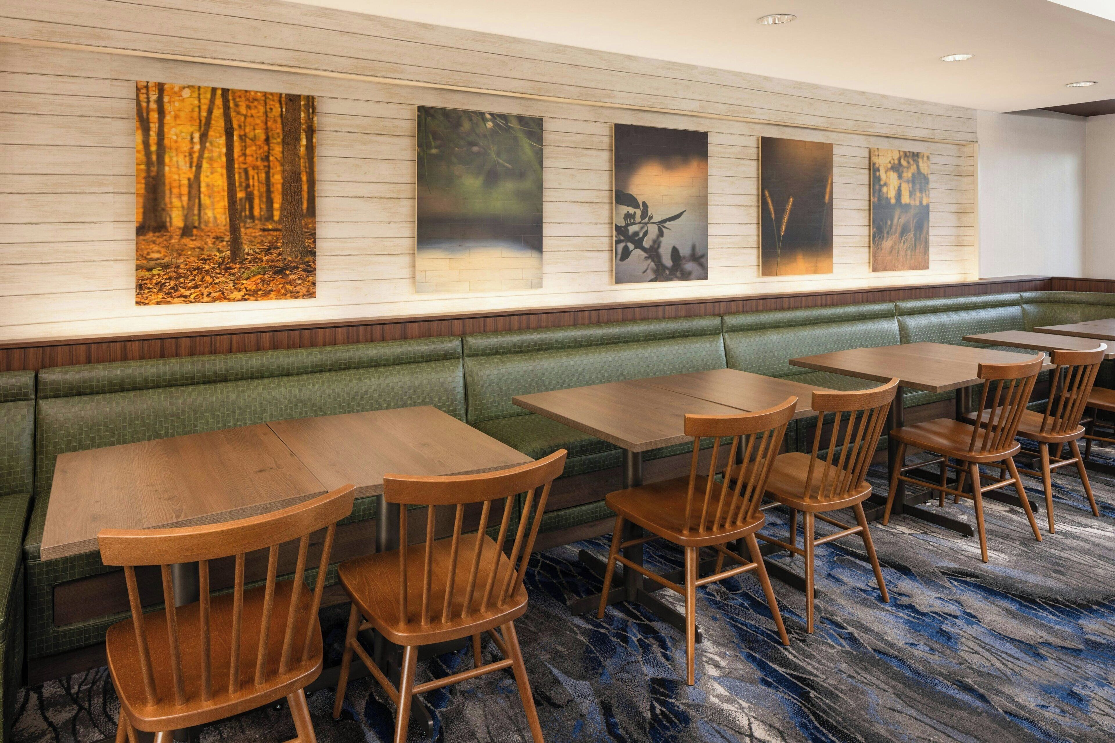 Un restaurante con mesas y sillas de madera, un banco con cojín verde y obras de arte en la pared.