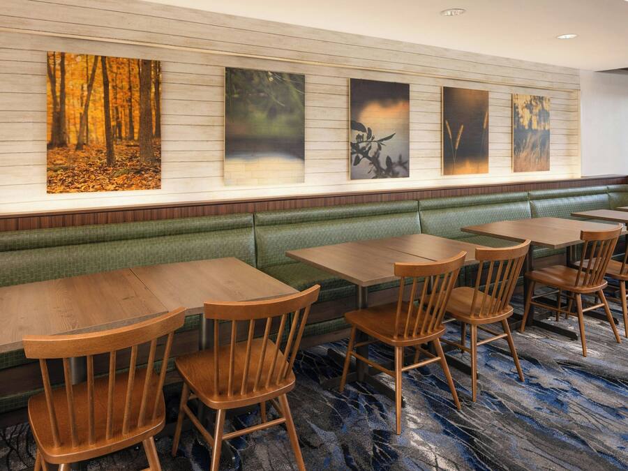 Un restaurante con mesas y sillas de madera, un banco con cojín verde y obras de arte en la pared.