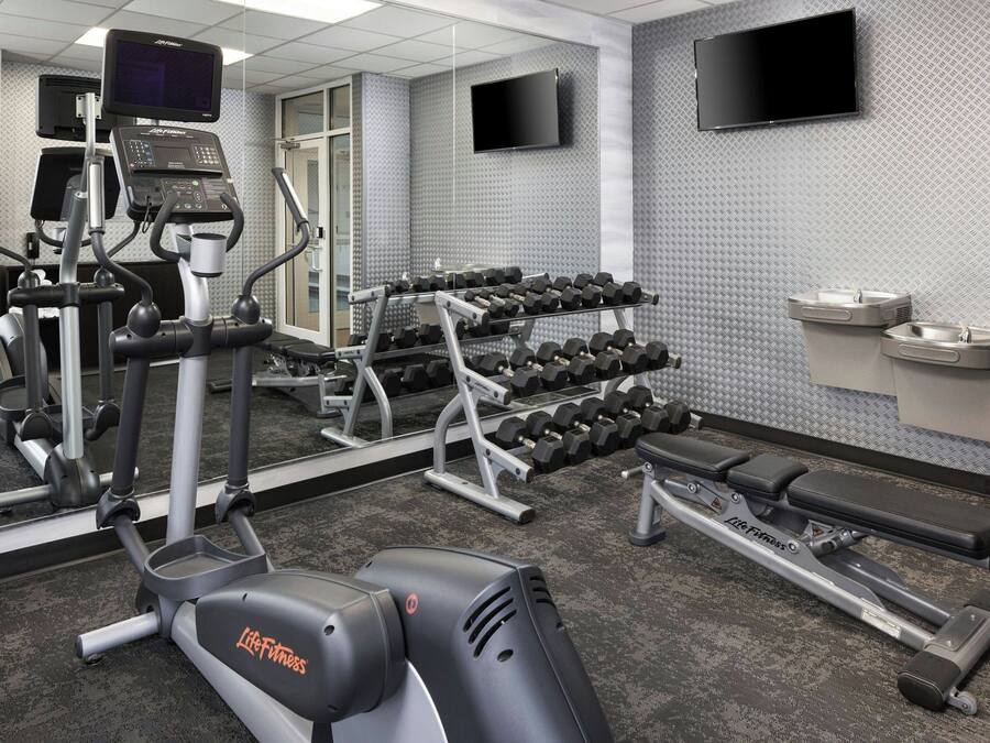 A gym with cardio machines, dumbbells, and a TV on the wall.