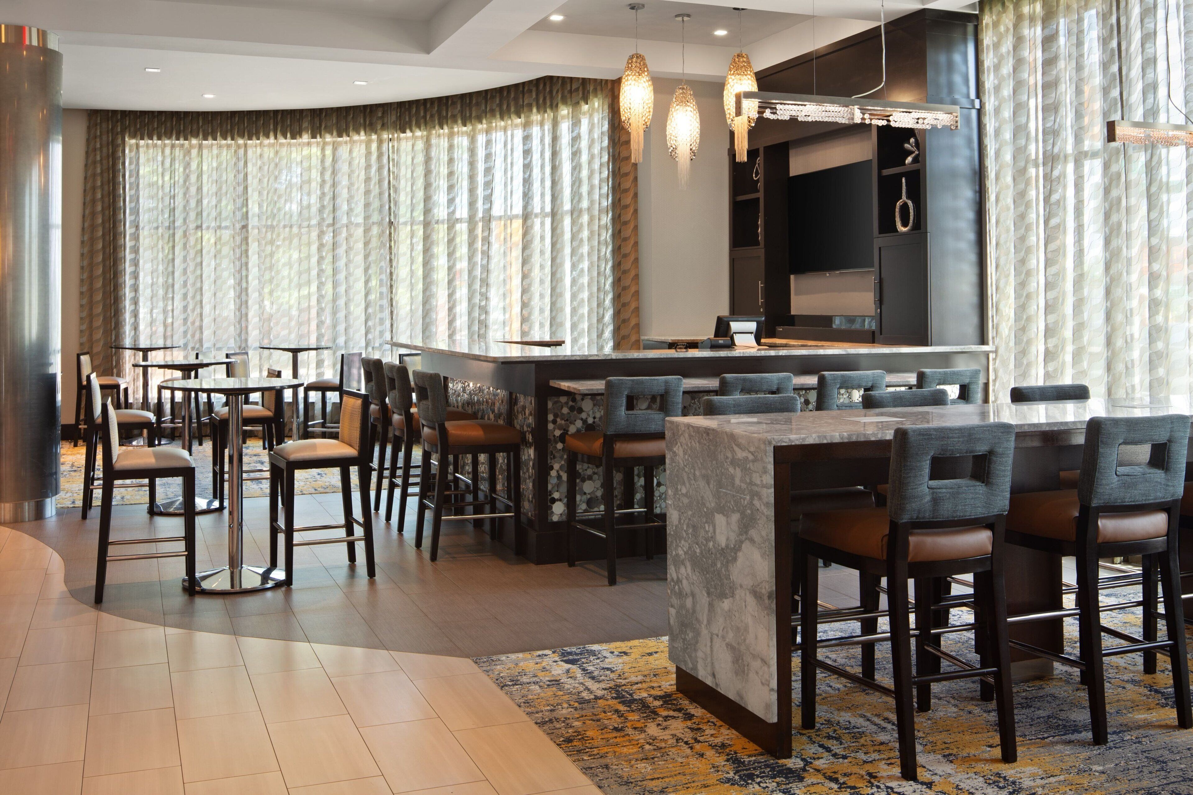 A modern bar area with a marble counter, bar stools, and pendant lighting.