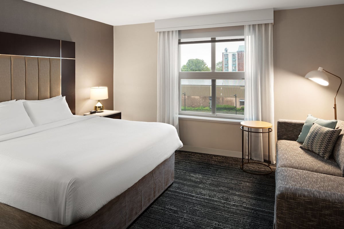 Une chambre d’hôtel avec un grand lit, une petite table ronde, un canapé et une fenêtre avec des rideaux.