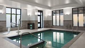 A modern indoor swimming pool with clear glass walls, a tiled floor, and a metal ladder.