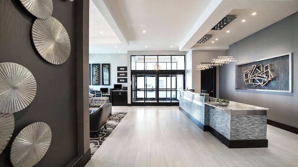 A modern hotel lobby with a reception desk, a large window, and decorative wall art.