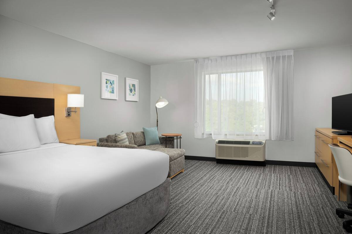 Ein Hotelzimmer mit einem großen Bett, einer Couch, einem Schreibtisch und einem Fernseher.