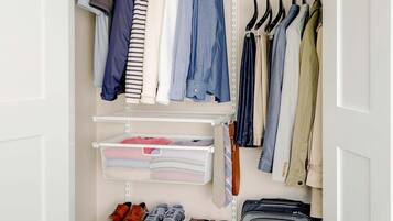 Um closet espaçoso com roupas penduradas, prateleiras com roupas dobradas, um sapateiro e uma mala.