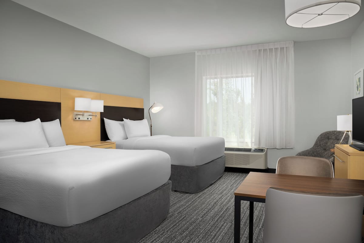 Ein Hotelzimmer mit zwei Betten, einem Schreibtisch, einem Stuhl, einem Fernseher und einem Fenster mit Vorhängen.