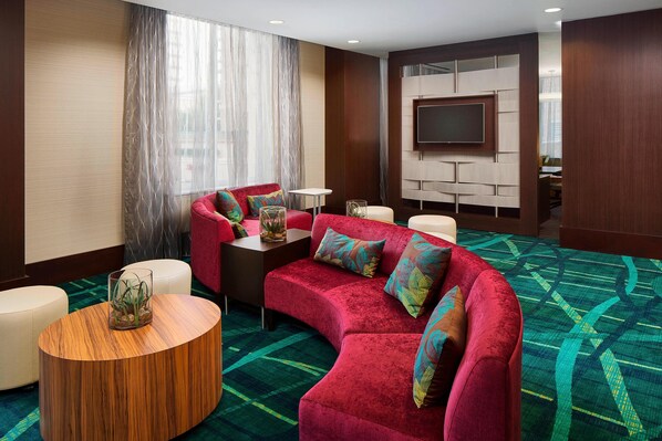 A modern hotel room with a red velvet sofa, a round wooden coffee table, and a flat-screen TV mounted on the wall. - Springhill Suites by Marriott Houston Dwntn/Convention Cntr (Houston)