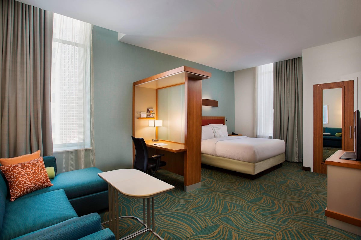 A hotel room with a bed, a desk, a chair, a sofa, and a small table.