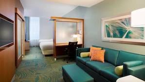 Une chambre d’hôtel avec un canapé vert, un bureau, une chaise, un lit et un téléviseur.