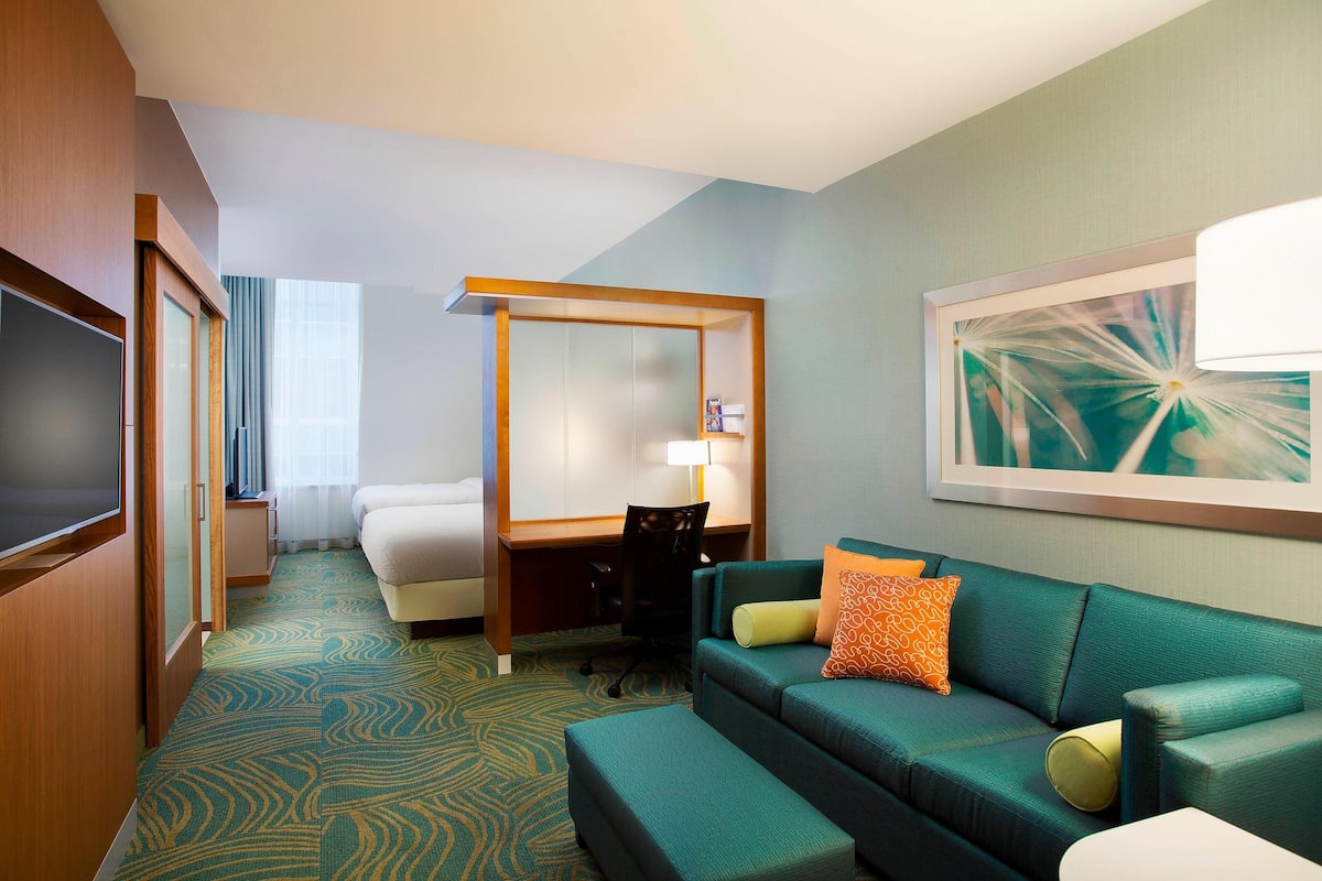 A hotel room with a green sofa, a desk, a chair, a bed, and a TV.