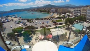 A coastal view from a high vantage point, featuring a marina with boats, a parking lot, and a beach area. - Atlantis Hotel (Agios Nikolaos)