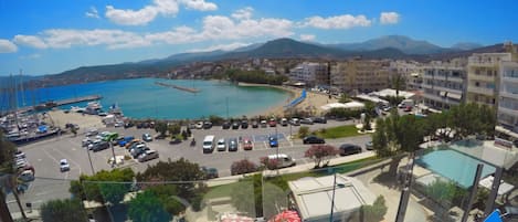 Vista costera desde un punto elevado, con un puerto deportivo, barcos, un estacionamiento y una zona de playa.