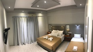 A hotel room with a large bed, a smaller bed, a desk, a mirror, and a window with curtains. - Atlantis Hotel (Agios Nikolaos)