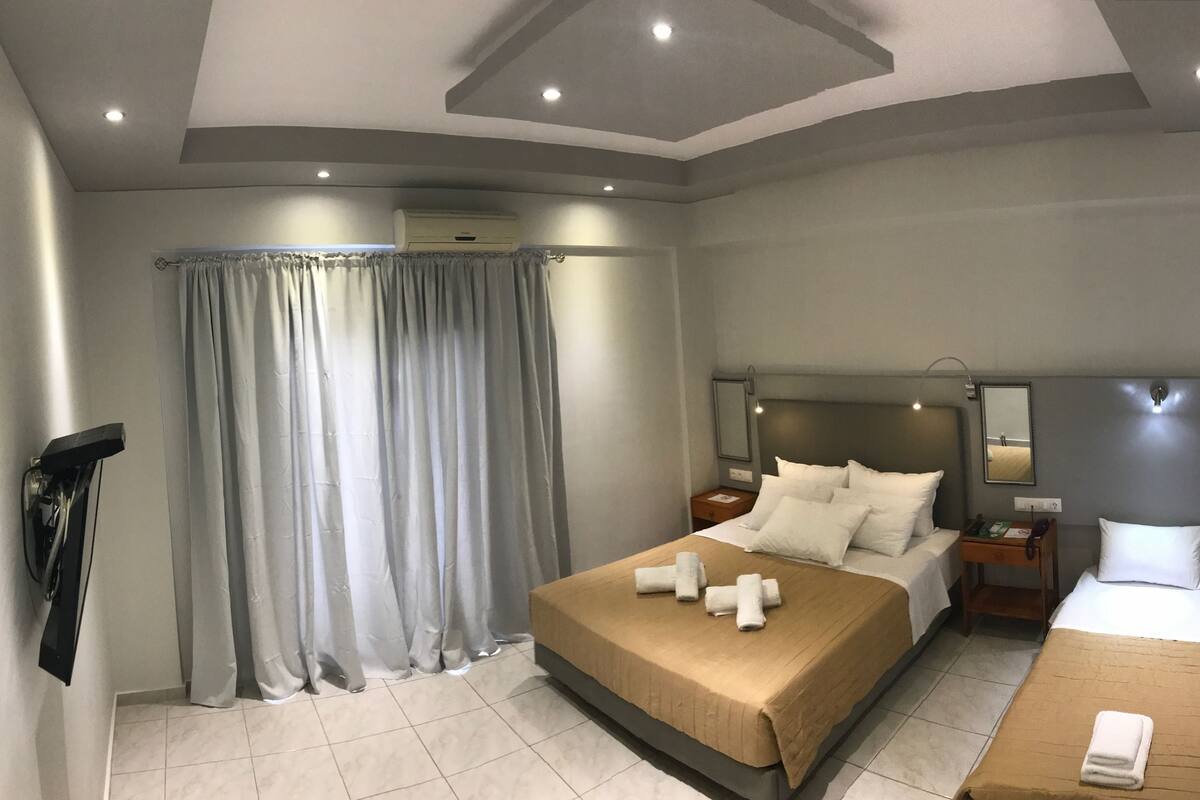 A hotel room with a large bed, a smaller bed, a desk, a mirror, and a window with curtains.