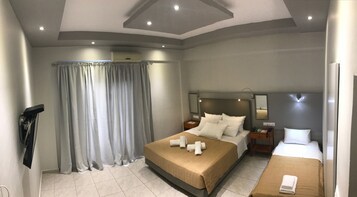 Habitación de hotel con una cama grande, una cama más pequeña, un escritorio, un espejo y una ventana con cortinas.