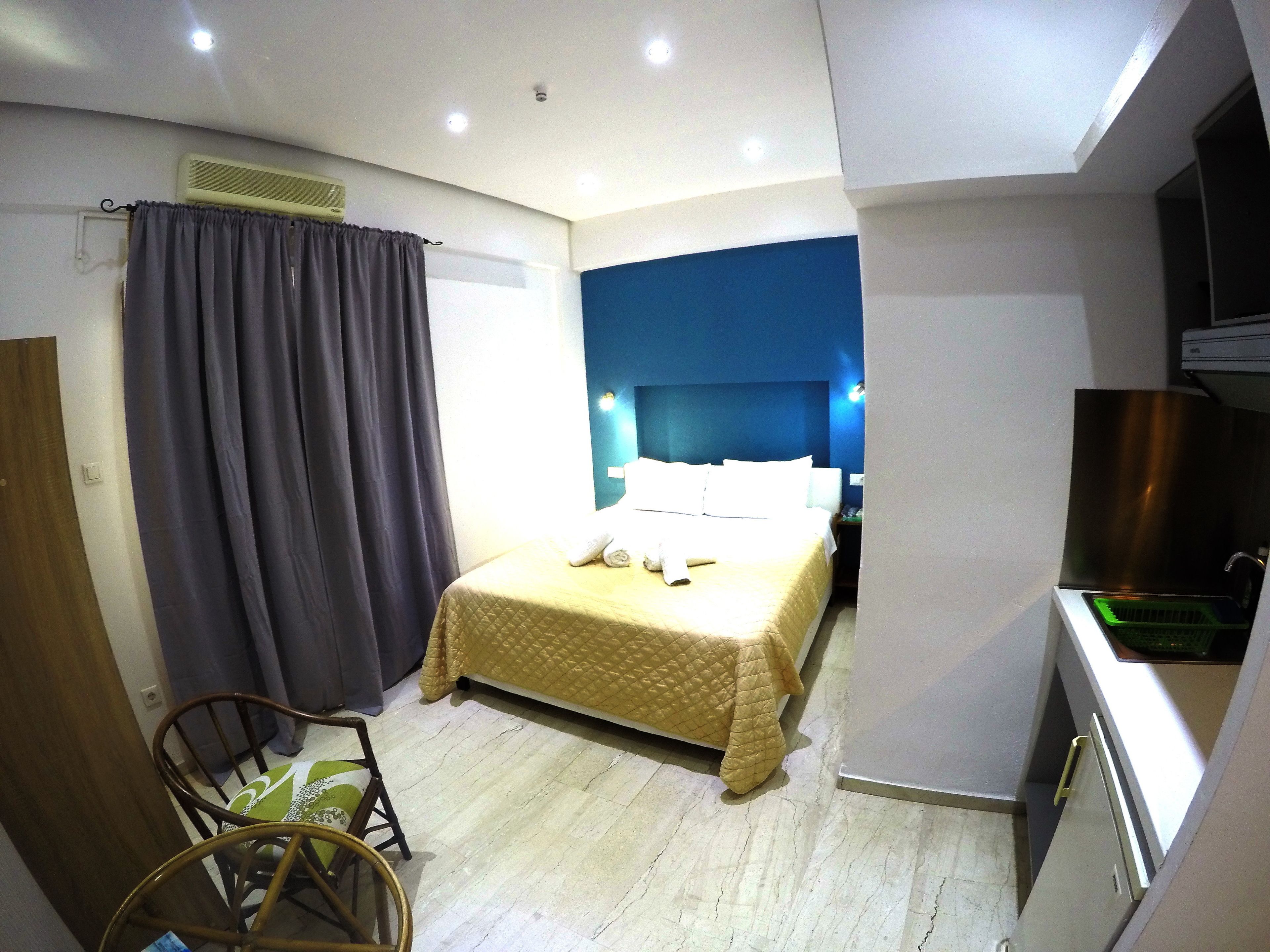 A compact hotel room with a bed, a chair, a kitchenette, and a bathroom.