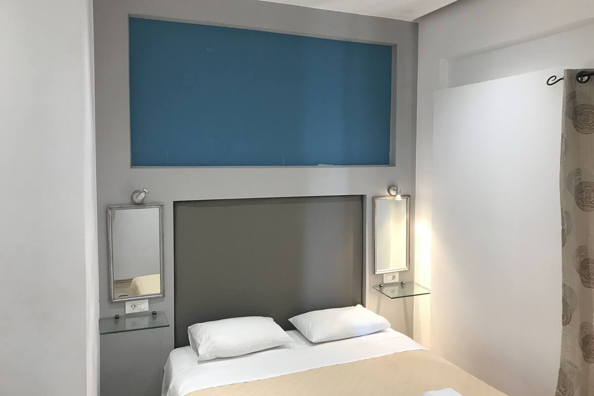 A hotel room with a bed, two bedside tables, a mirror, and a wall-mounted light fixture.