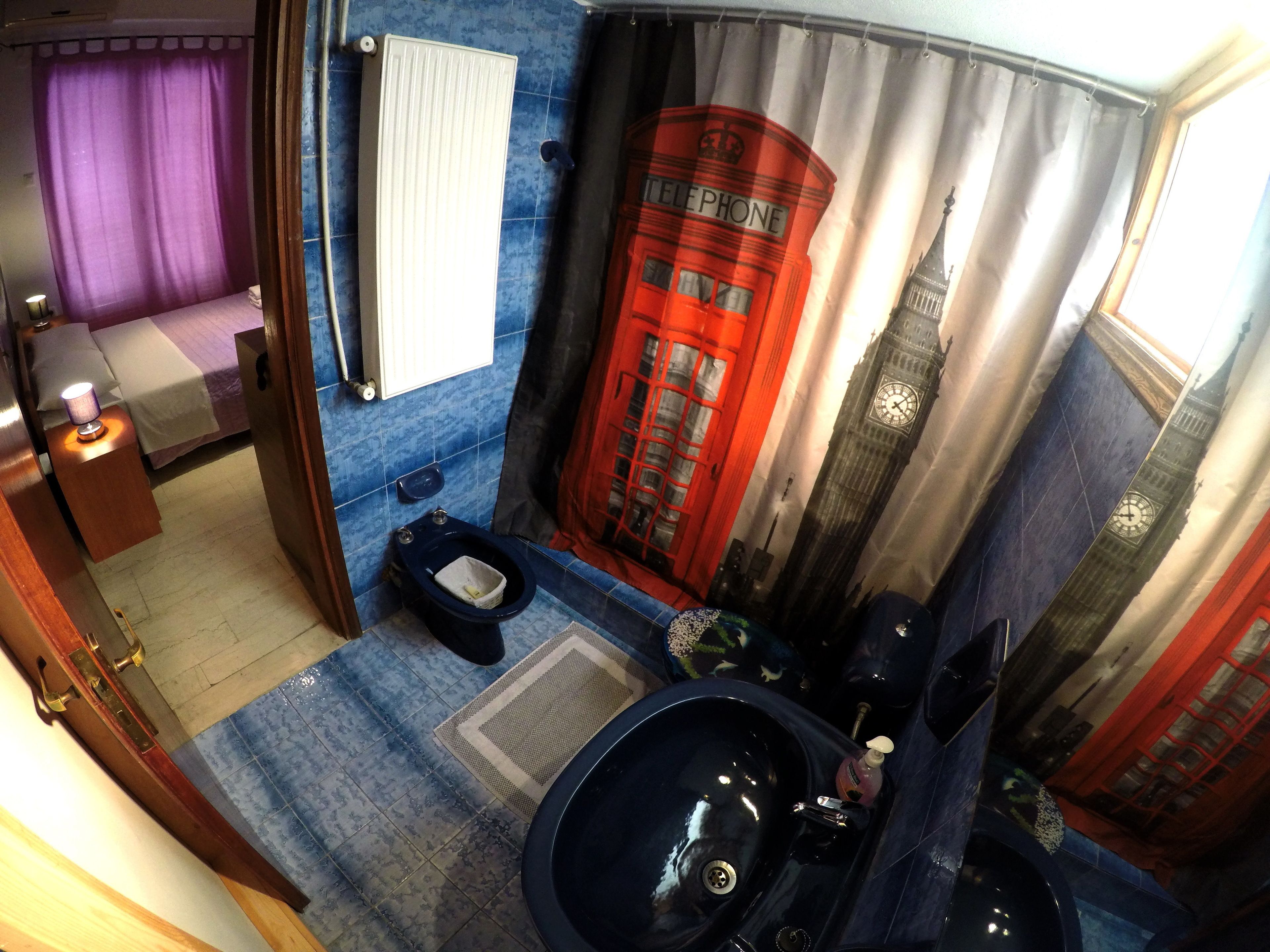 Une salle de bain avec un sol carrelé de carreaux bleus, un lavabo noir, des toilettes et un miroir.