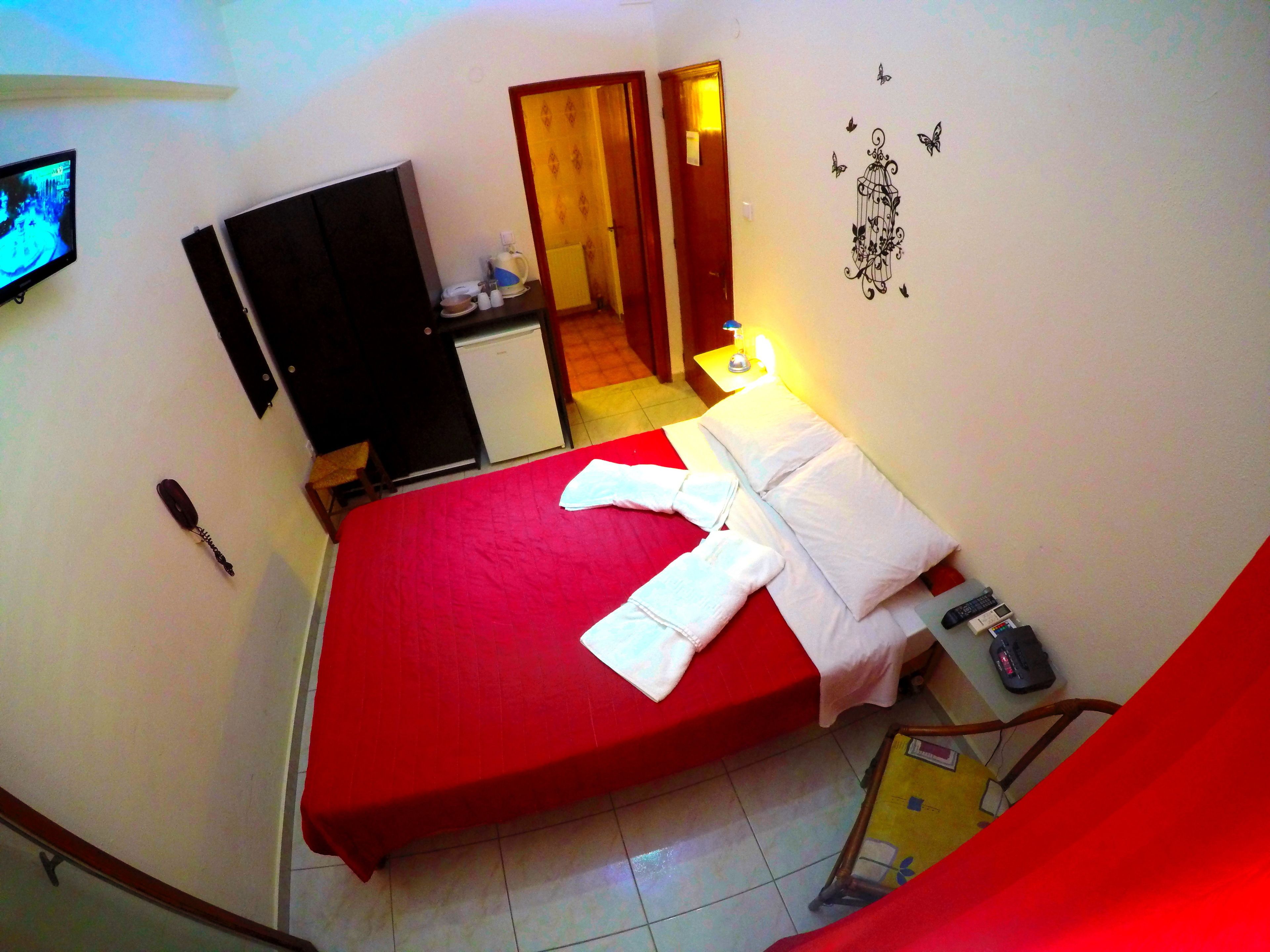 A hotel room with a red bedspread, a television, a desk with a lamp, and a small refrigerator.