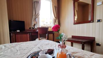 Una habitación de hotel con una cama, televisión, una mesa de comedor y una bandeja de desayuno, un florero y un espejo.