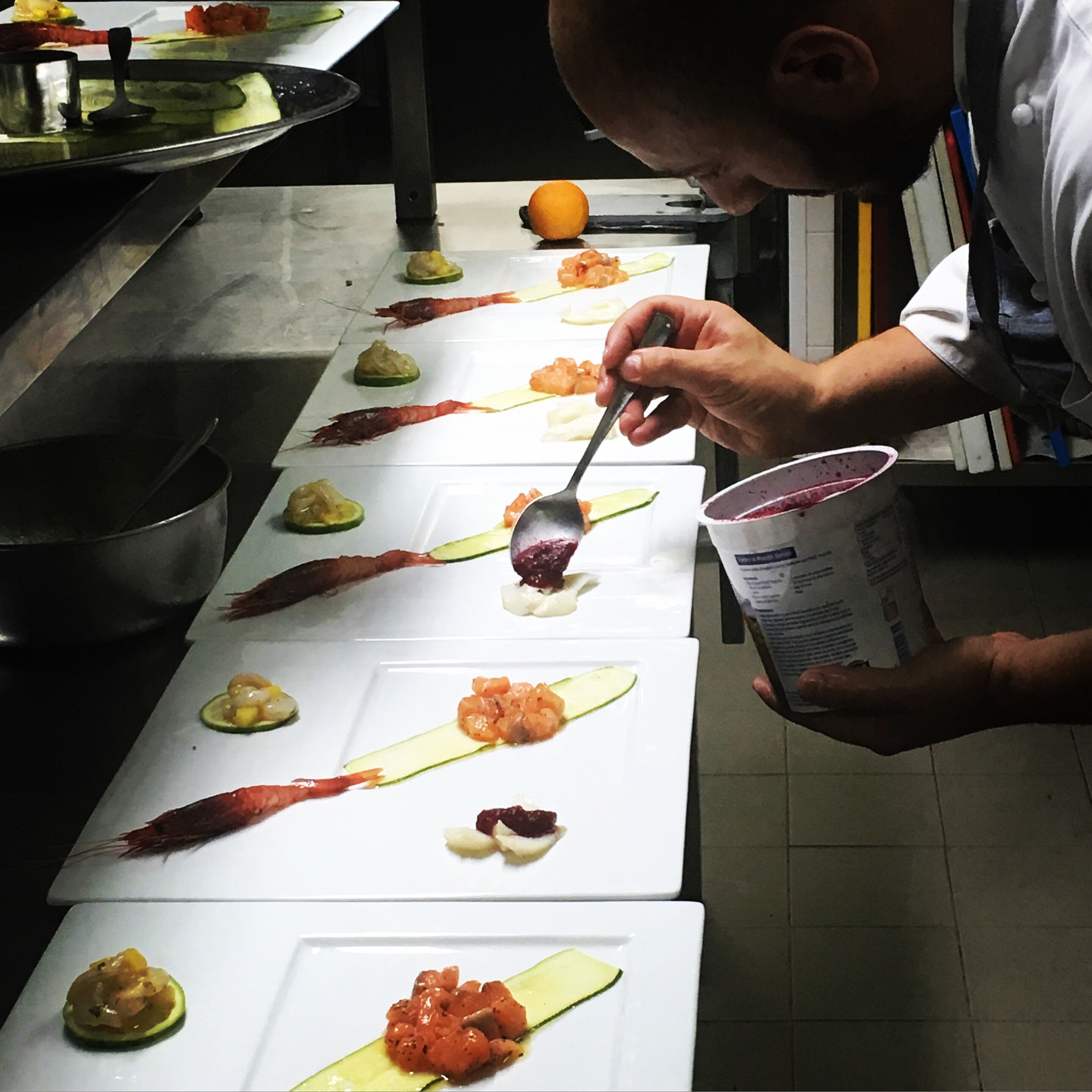 Un chef prépare des plats sur une longue table blanche dans une cuisine.