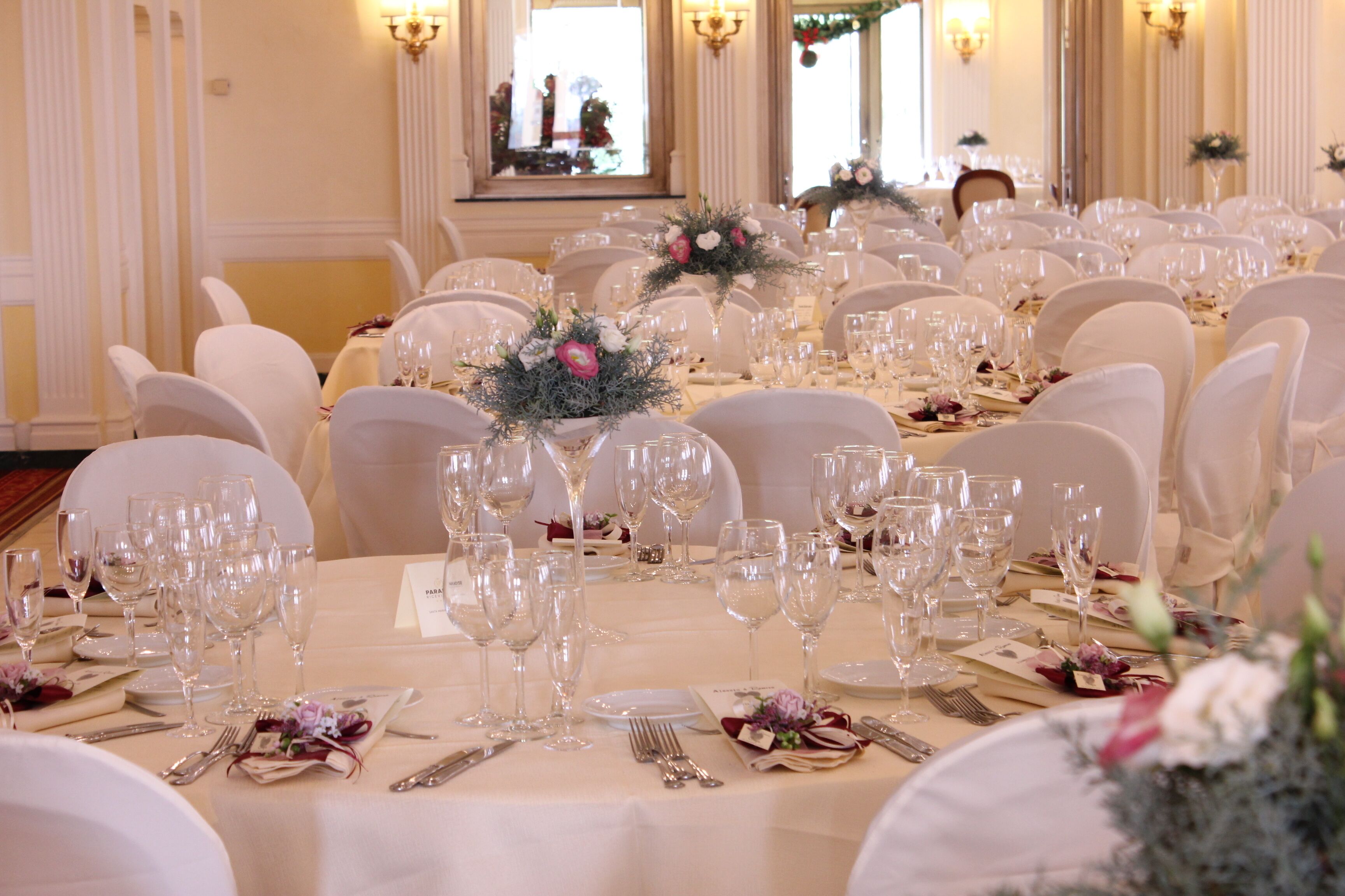 A banquet hall with round tables set for a formal event, featuring white tablecloths, glassware, and floral centerpieces.