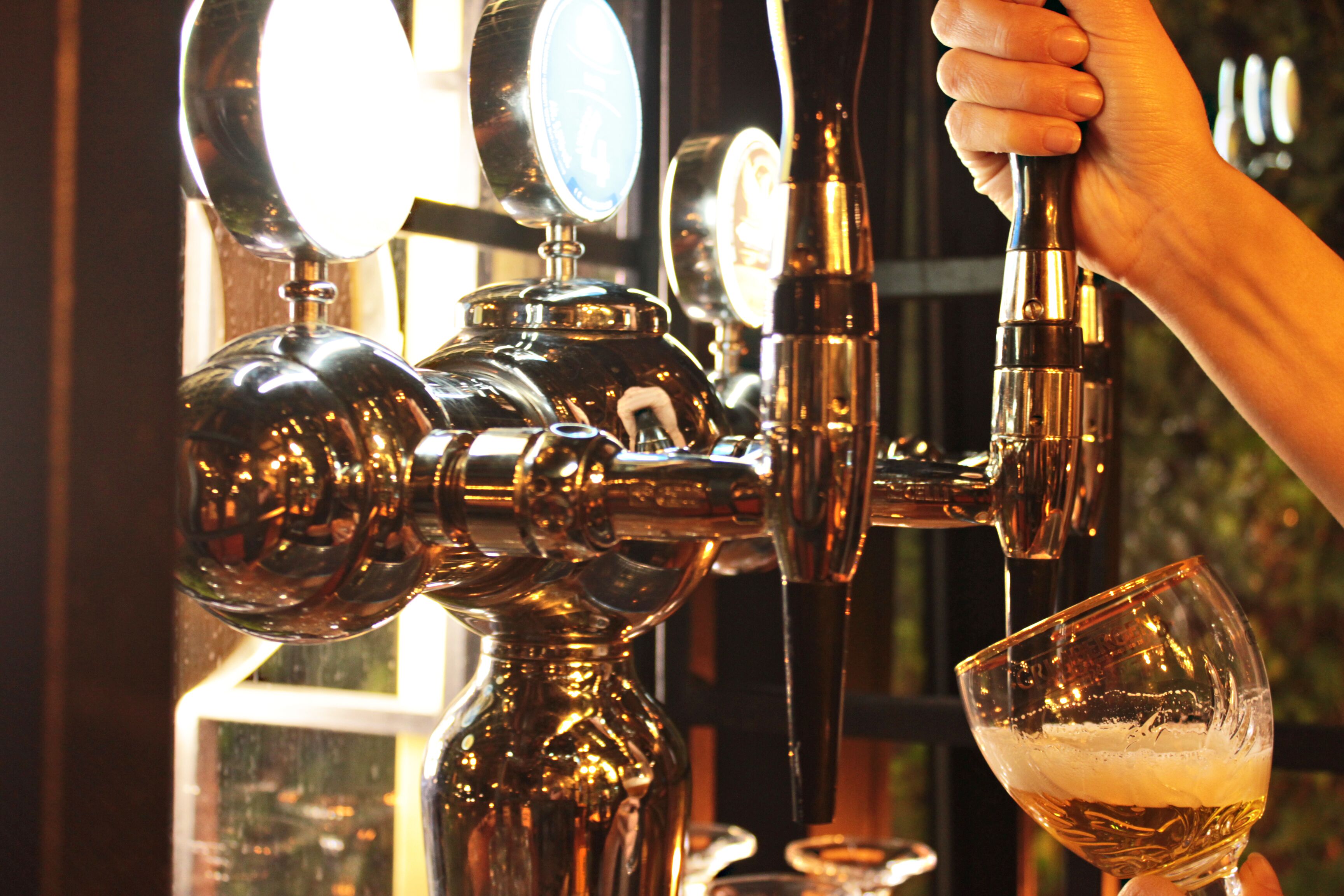A hand holding a beer tap, pouring beer into a glass.