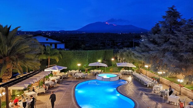 Zona junto a la piscina con mesas y sillas, piscina y vista a una montaña con un volcán al fondo.