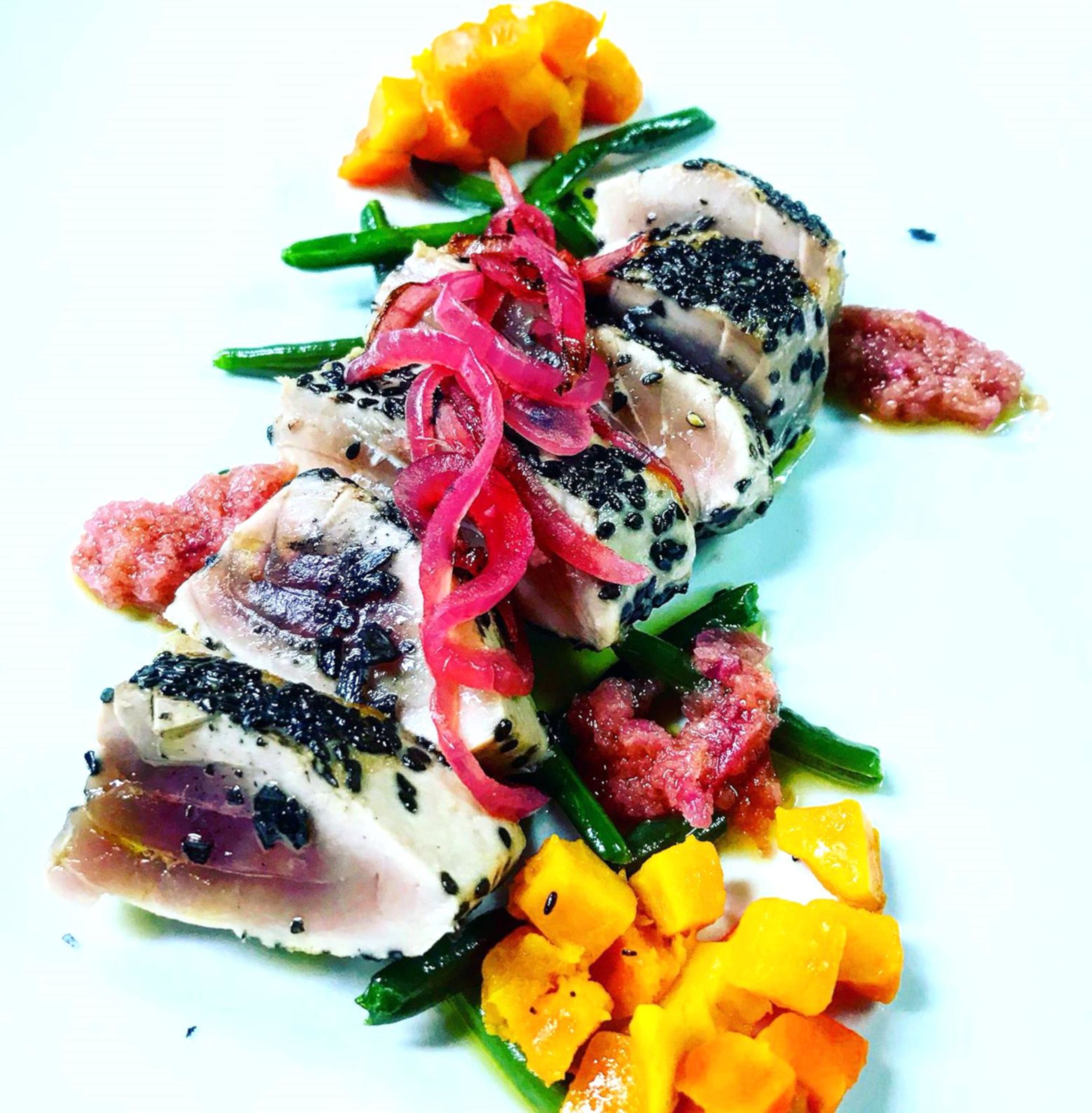 Ein Teller mit Fischscheiben, roten Zwiebeln und Mango.