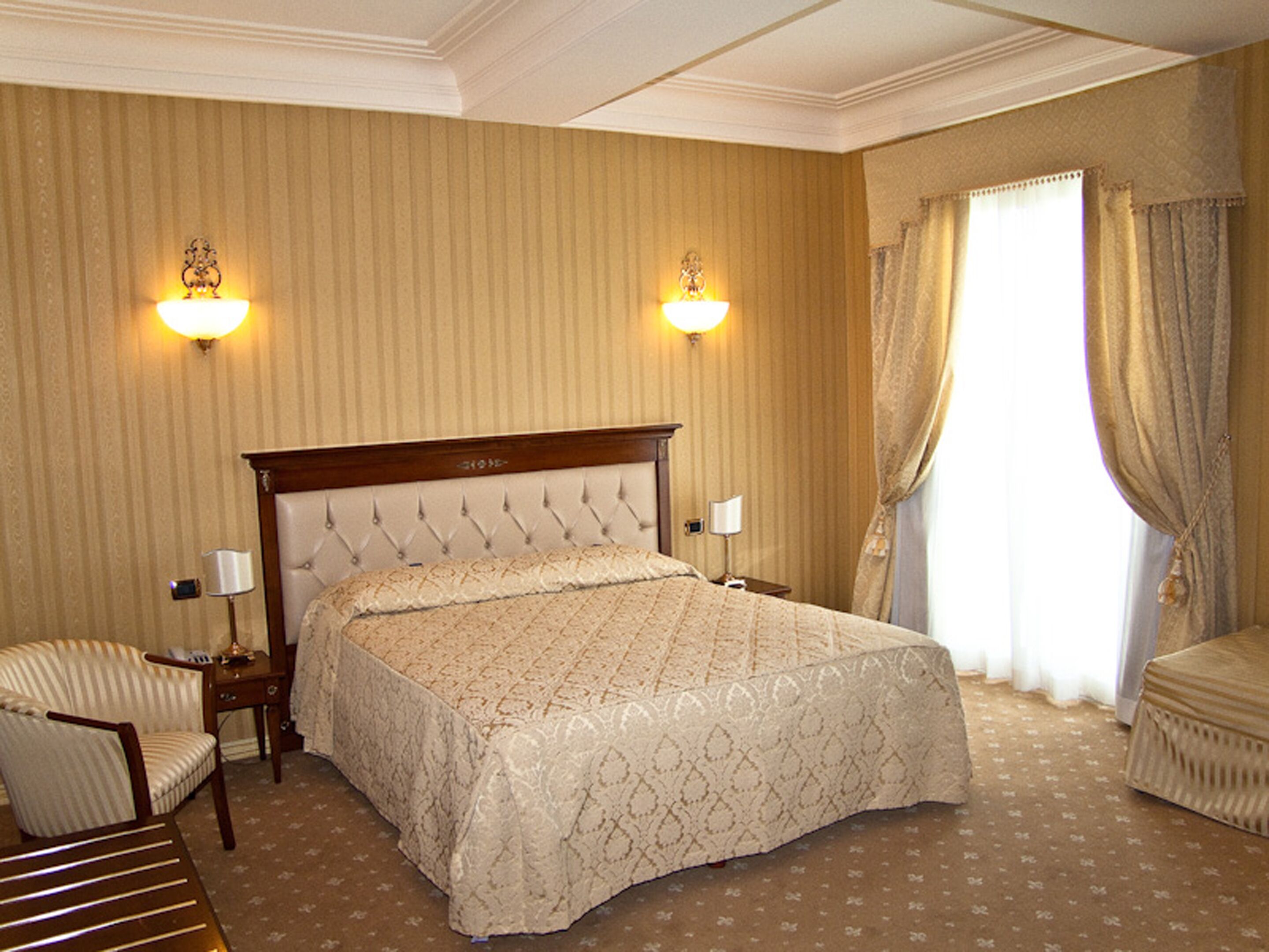 A hotel room with a large bed, two bedside lamps, a chair, and a window with curtains.