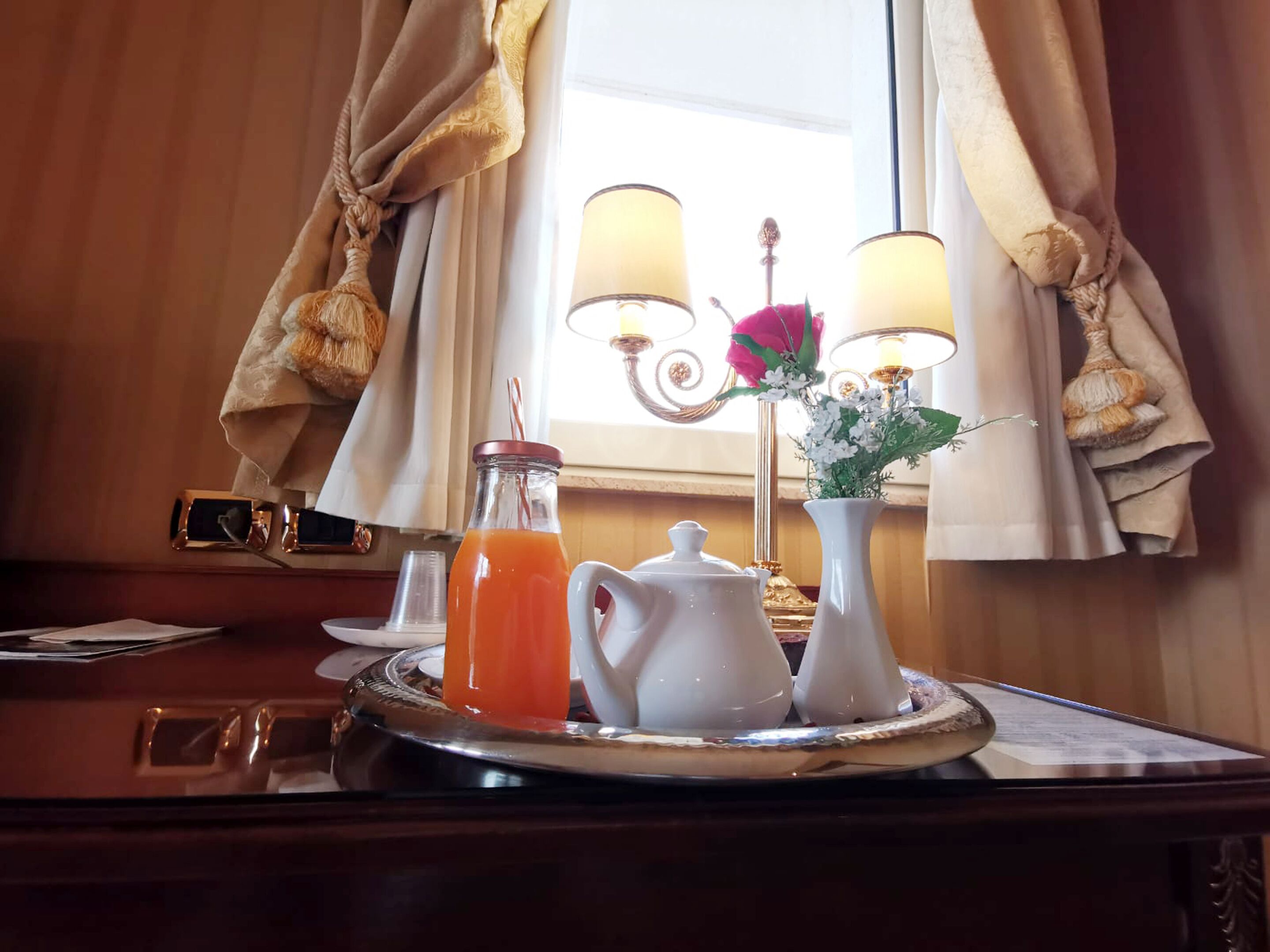 Ein Frühstücksbrett mit Orangensaft, einem Teekännchen und einer Zuckerdose auf einer Holztischplatte.