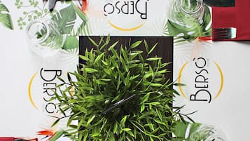 Mesa posta com um arranjo verde, toalha branca e guardanapos vermelhos.