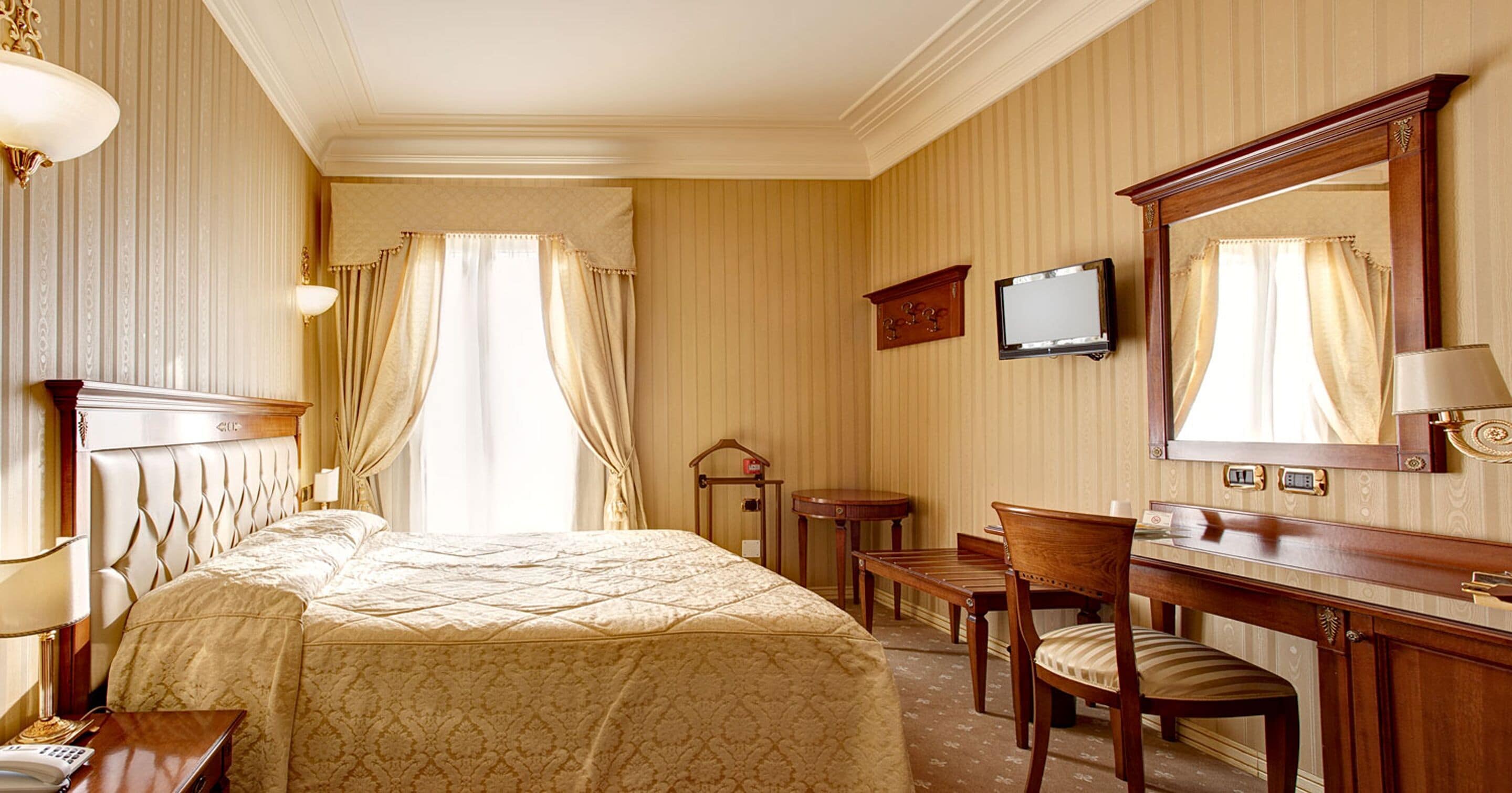 Una habitación de hotel con una cama grande, un escritorio con silla, televisión y espejo.