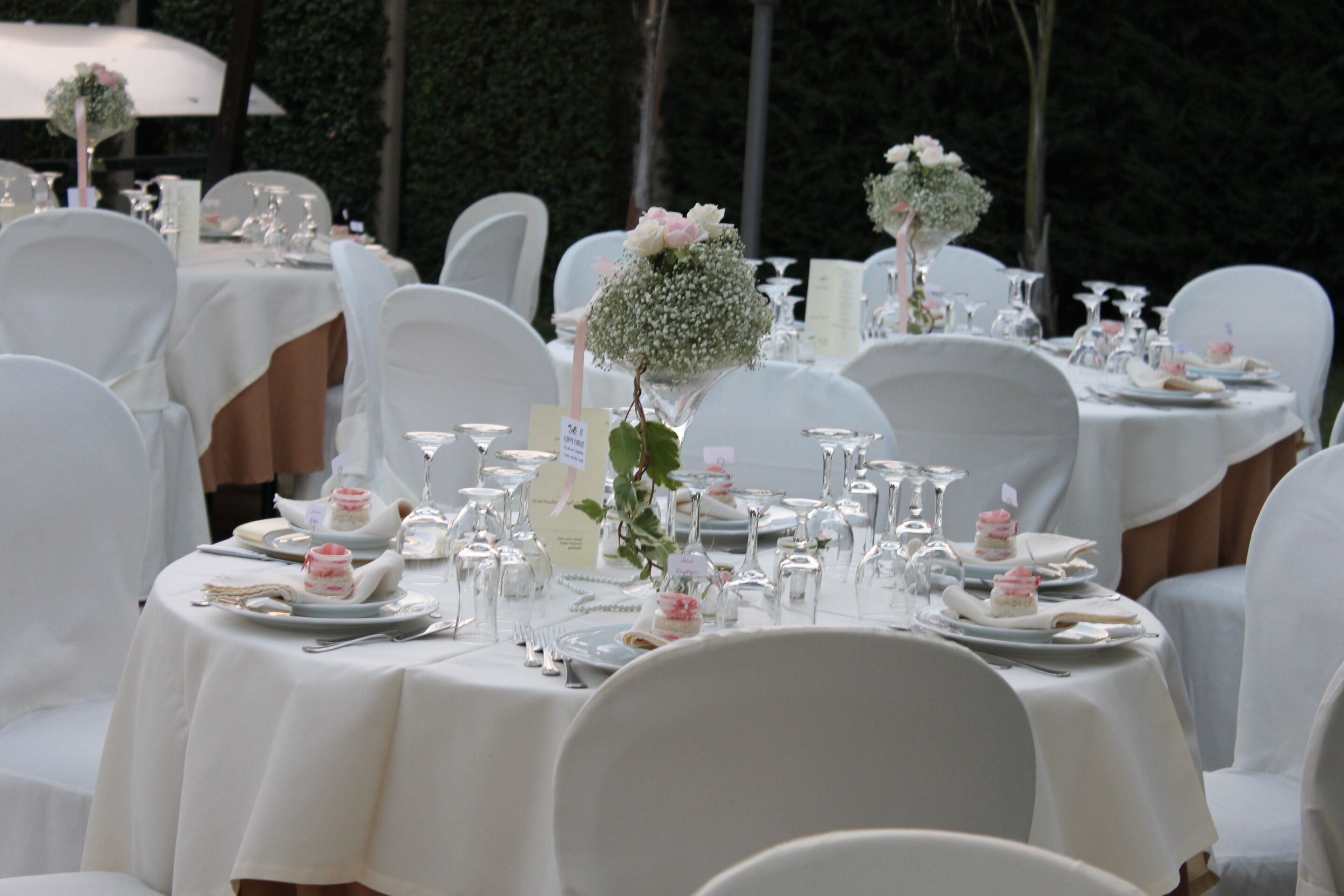 Een feestzaal met ronde tafels gedekt voor een formeel evenement, voorzien van witte tafellakens, servies en bloemstukken.