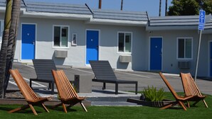 Un motel aux portes et fenêtres bleues, avec des espaces extérieurs aménagés de chaises en bois, et un panneau indiquant un stationnement payant avec un montant minimal d’amende.