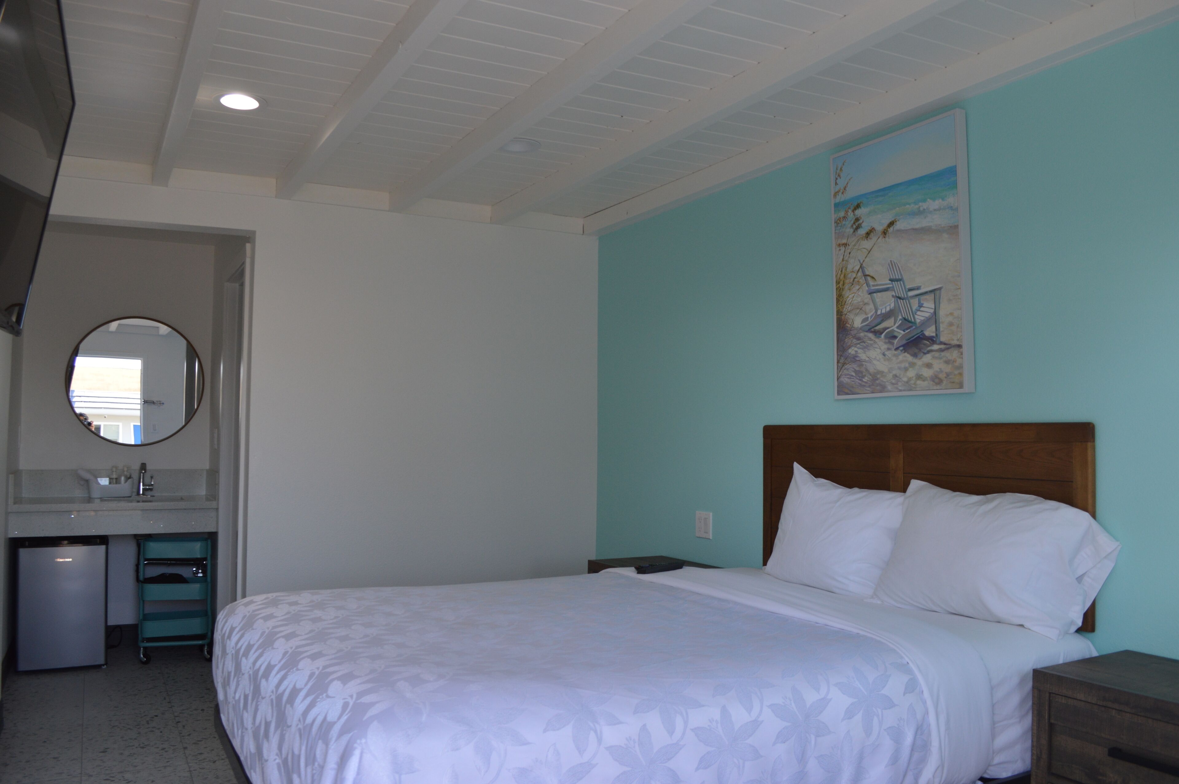 Ein Hotelzimmer mit einem Bett, einem kleinen Schreibtisch, einem Spiegel und einem Bild mit einer Strandansicht.