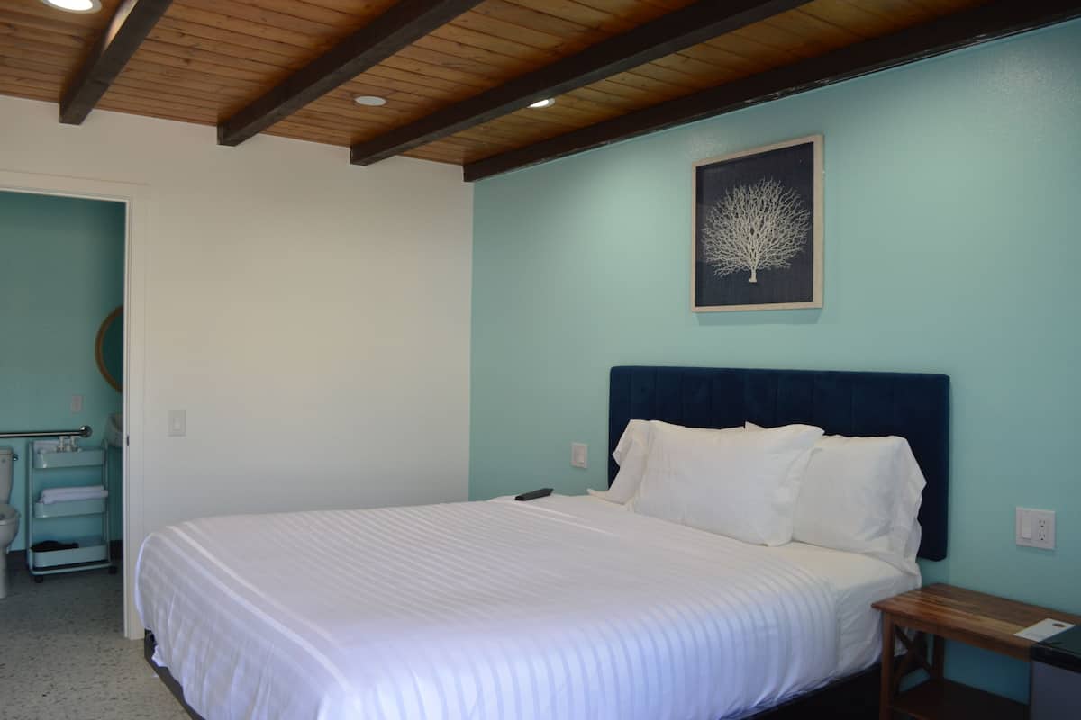 A bedroom with a bed, a headboard, a wall-mounted artwork, a bedside table, and a bathroom with a toilet and a towel rack.