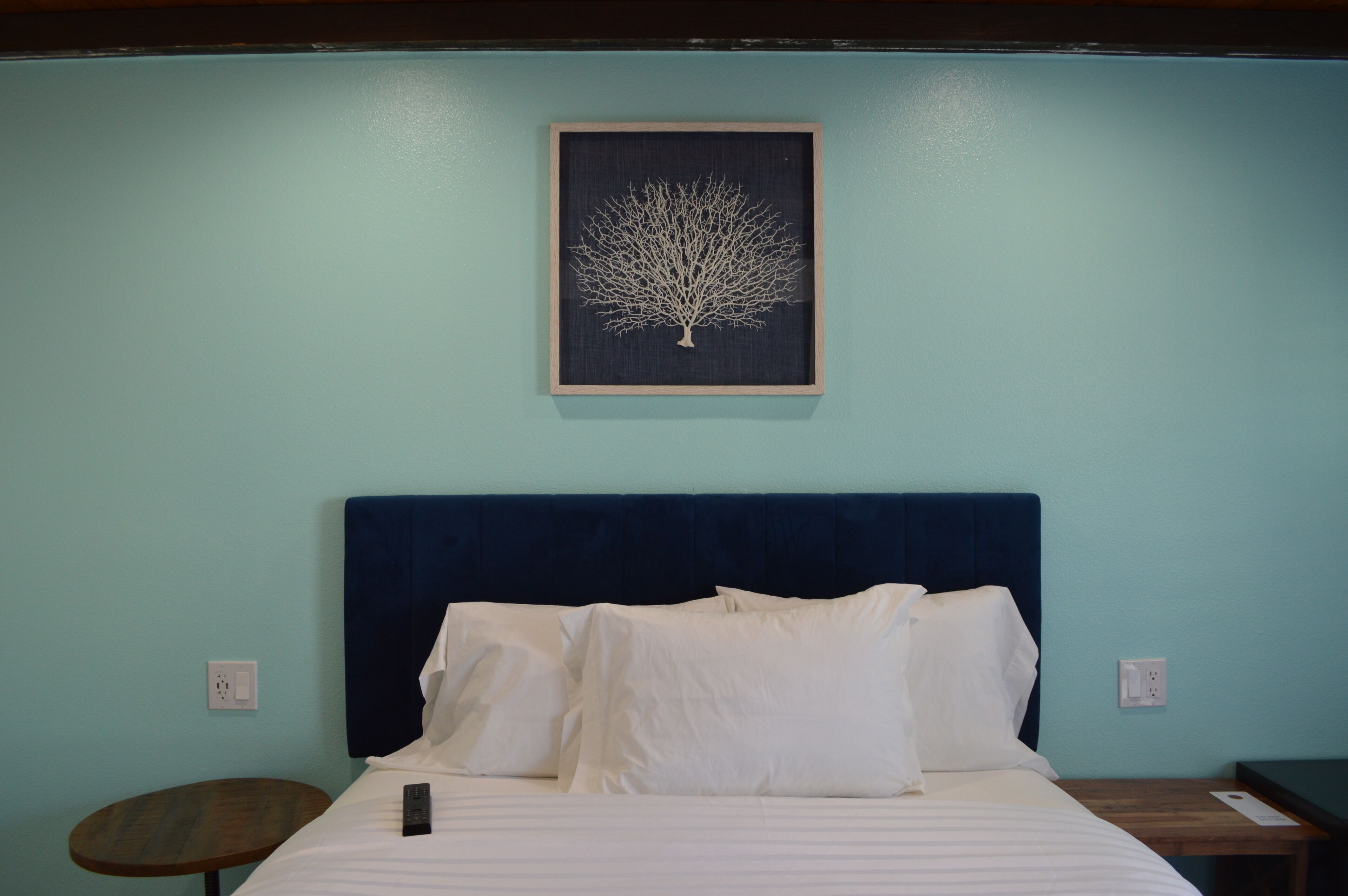 Una cama bien tendida con sábanas blancas y un cabecero azul oscuro en una habitación con paredes azul cielo.