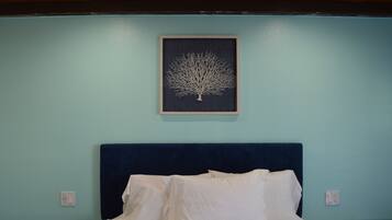 Una cama bien tendida con sábanas blancas y un cabecero azul oscuro en una habitación con paredes azul cielo.