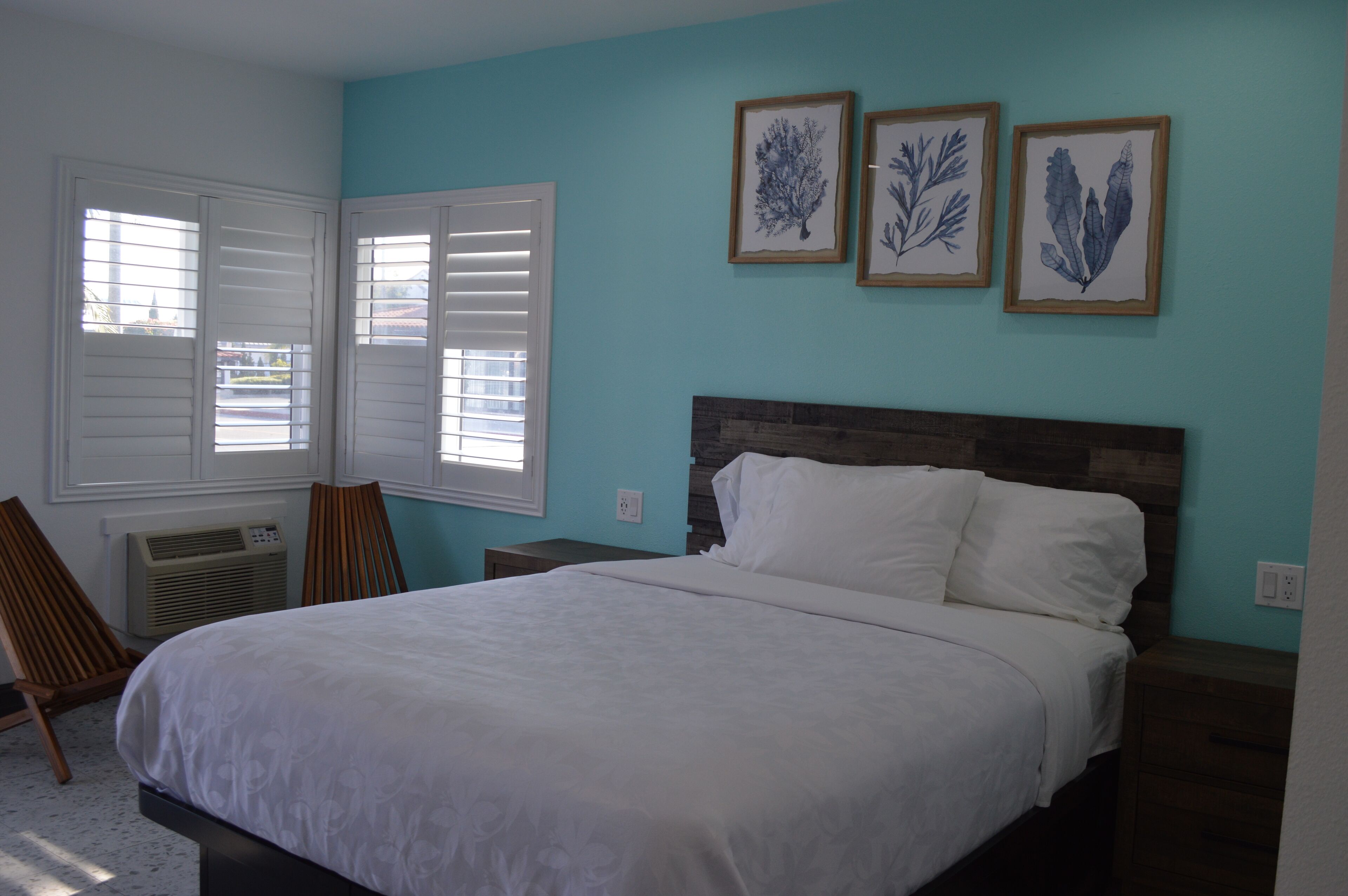 Quarto com cama, cadeira, mesa de cabeceira e ar condicionado fixado na parede.