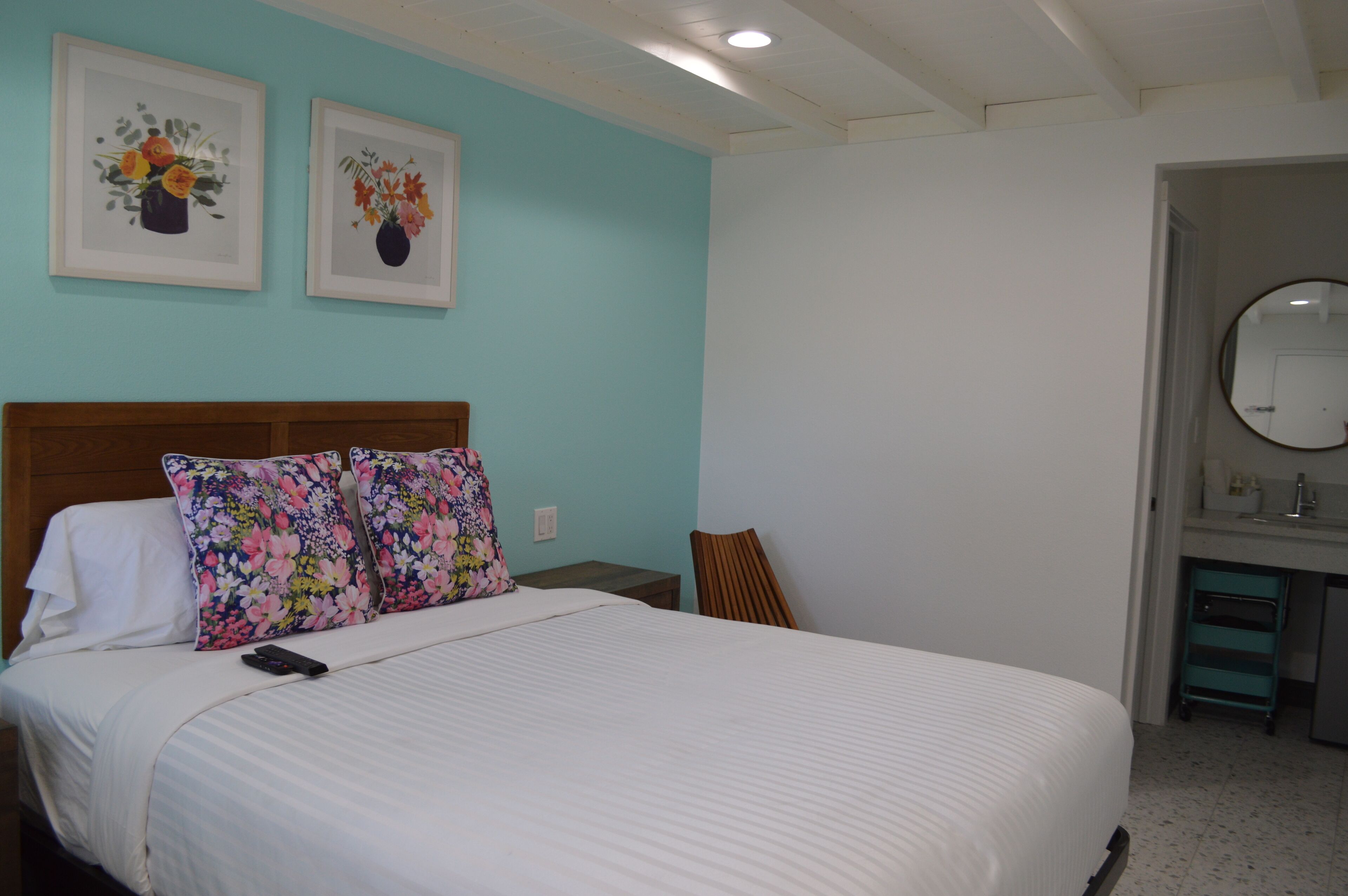 Una cama bien hecha con un control remoto, un cabecero de madera y dos almohadas estampadas con motivos florales.