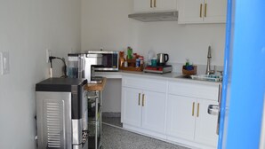 Une cuisine compacte avec des meubles blancs, un four à micro-ondes, une machine à café et un petit réfrigérateur.