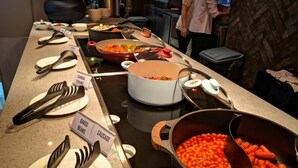 A buffet setup with labeled dishes including baked beans and sausage, and a chef preparing food in the background. - King Park Hotel Kota Kinabalu (Kota Kinabalu)